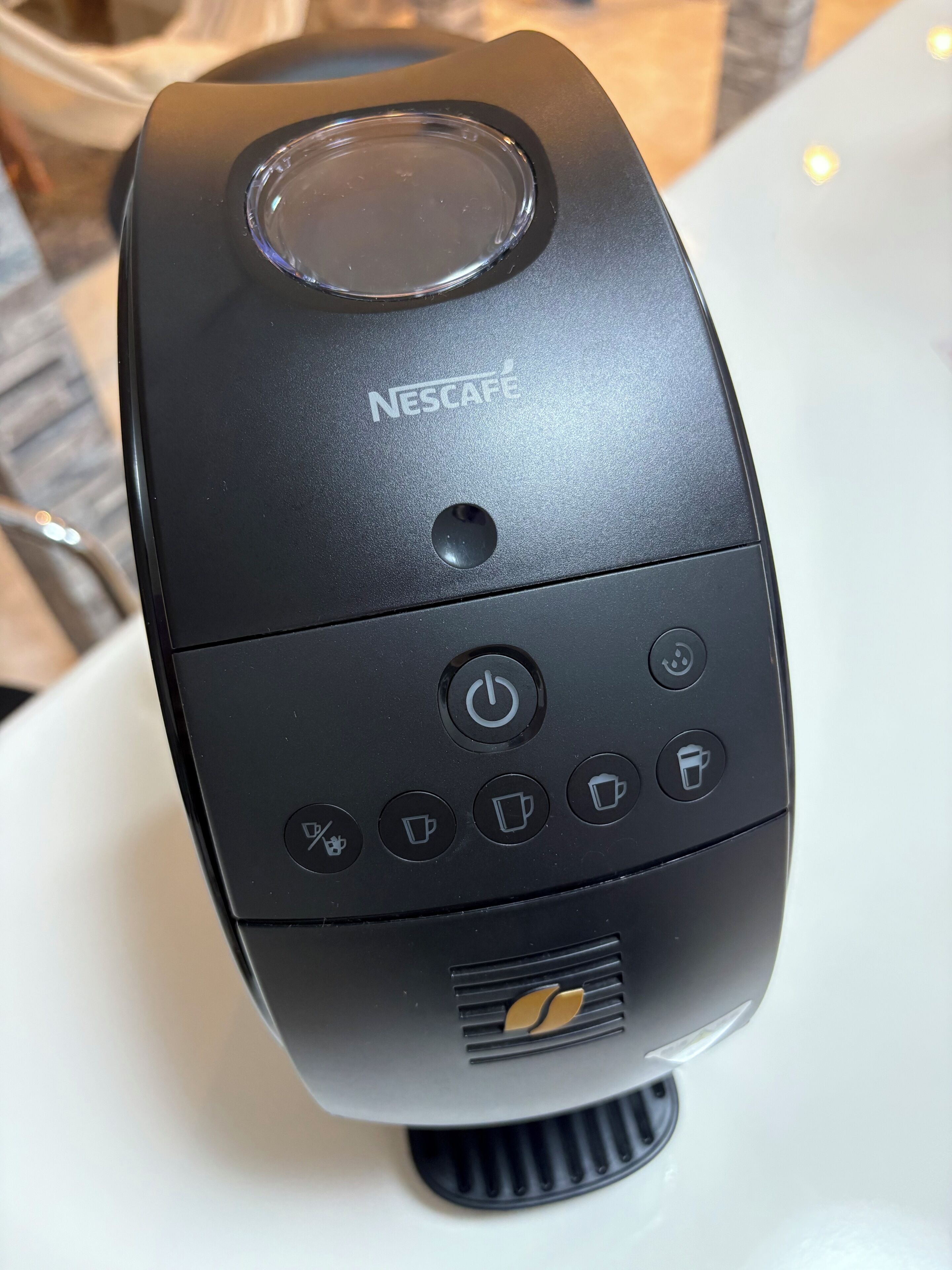 A black Nescafe coffee machine with a power button, a coffee cup icon, a cup icon, a cup of coffee icon, and a cup of espresso icon.