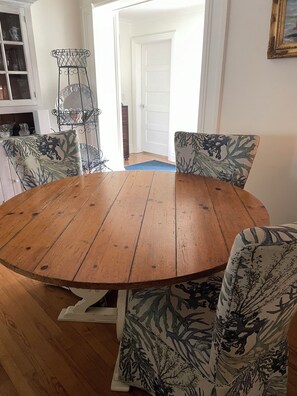 Een ronde houten eettafel met vier stoelen, elk voorzien van een kussen met bladmotief.