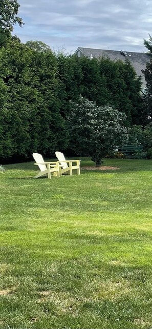 A grassy area with two white chairs and a small table, surrounded by dense green foliage and a building in the background. - THE PERFECT SUMMER HOME Tranquil 3-bedrooms home in charming Rumson NJ (Rumson)
