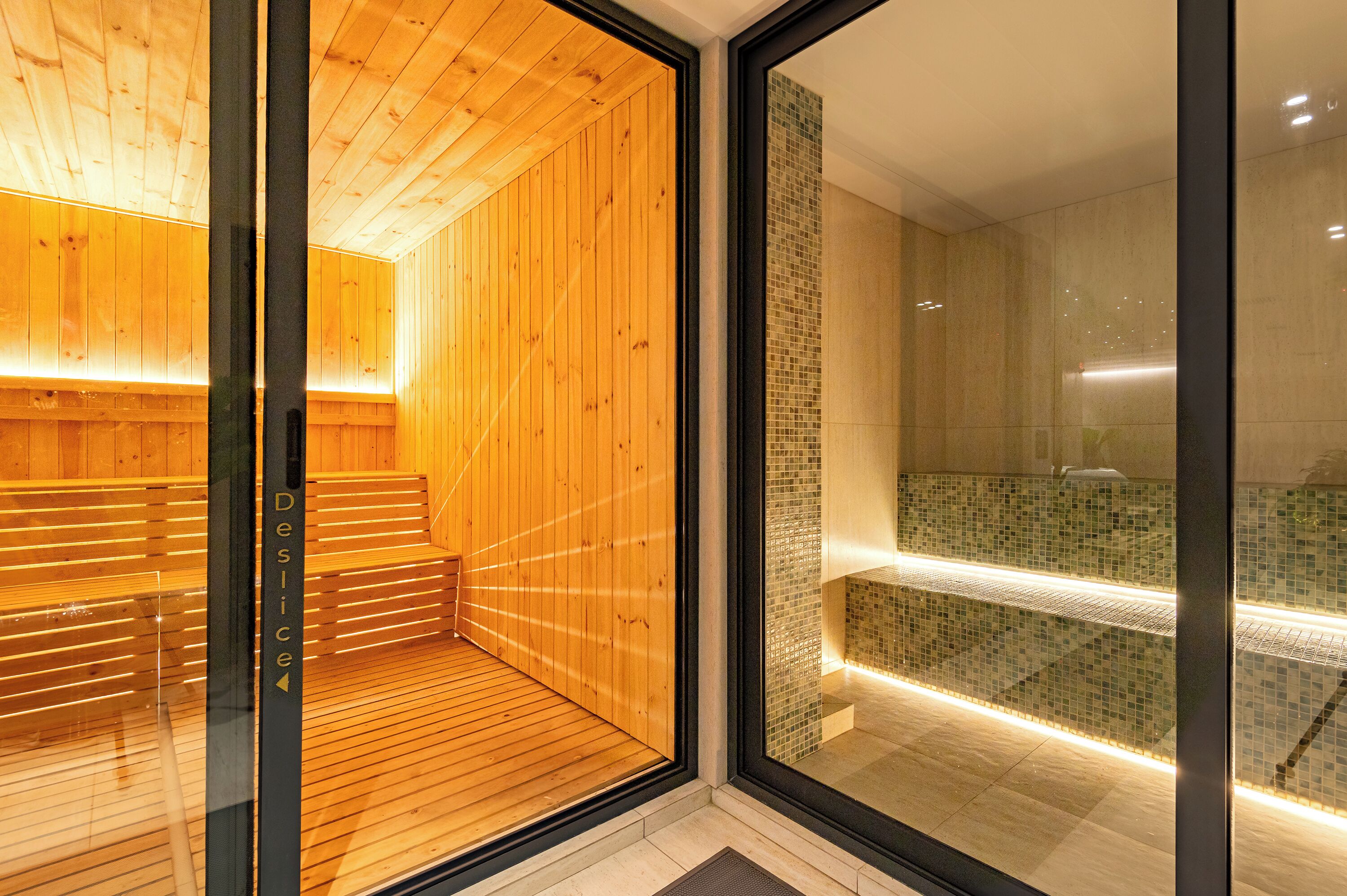 A modern sauna with wooden walls and a glass door, leading to a tiled shower area.
