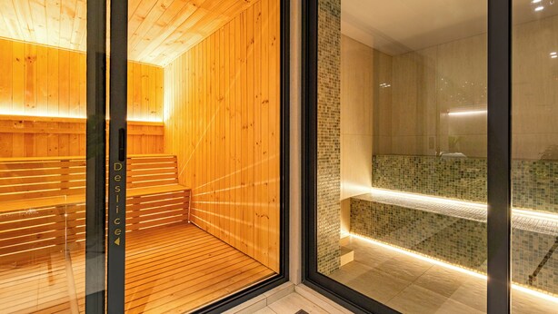 En moderne sauna med trævægge og en glasdør, der fører til et fliset badeområde.