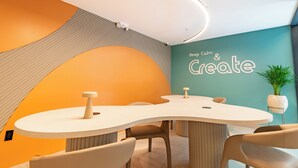 Et moderne mødelokale med et buet bord, komfortable stole, en potteplante og en væg med teksten 'Keep Calm & Create'.