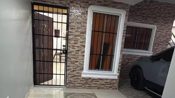 Un corridoio con pavimento piastrellato, una porta con inferriata metallica e una finestra con cornice bianca.