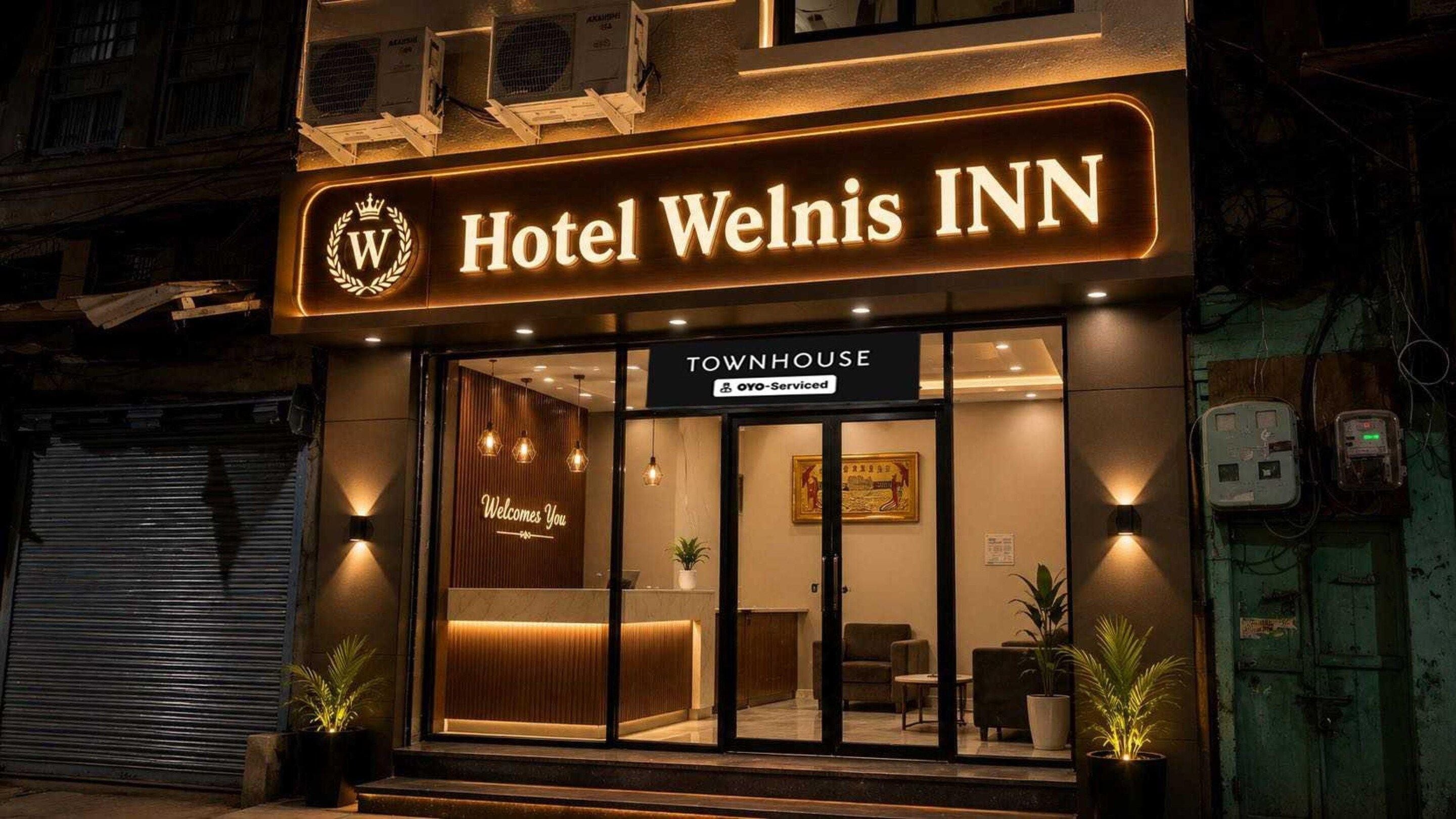 L’hôtel Welnis INN, reconnaissable à son panneau « Townhouse », dispose d’une réception et d’un panneau d’accueil indiquant « Bienvenue ».