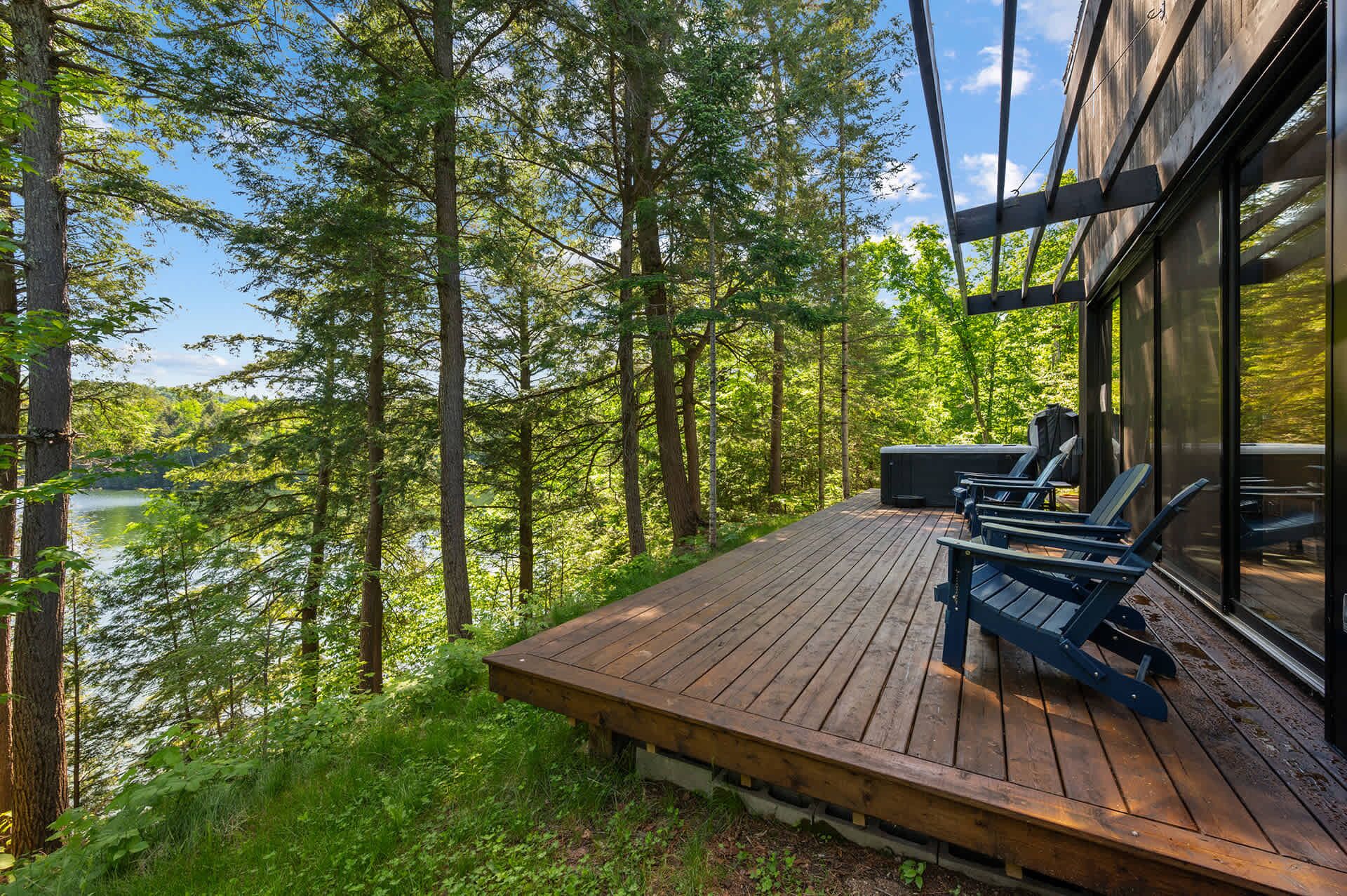 A wooden deck with outdoor seating, overlooking a forested area and a body of water.