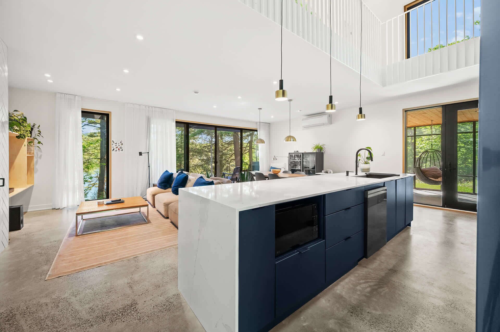 A modern kitchen with a central island, large windows, and a hanging chair.
