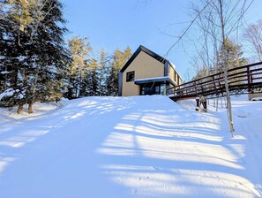 A modern building with a sloped roof, surrounded by snow-covered ground and trees. - Ambre (Grenville-sur-la-Rouge)