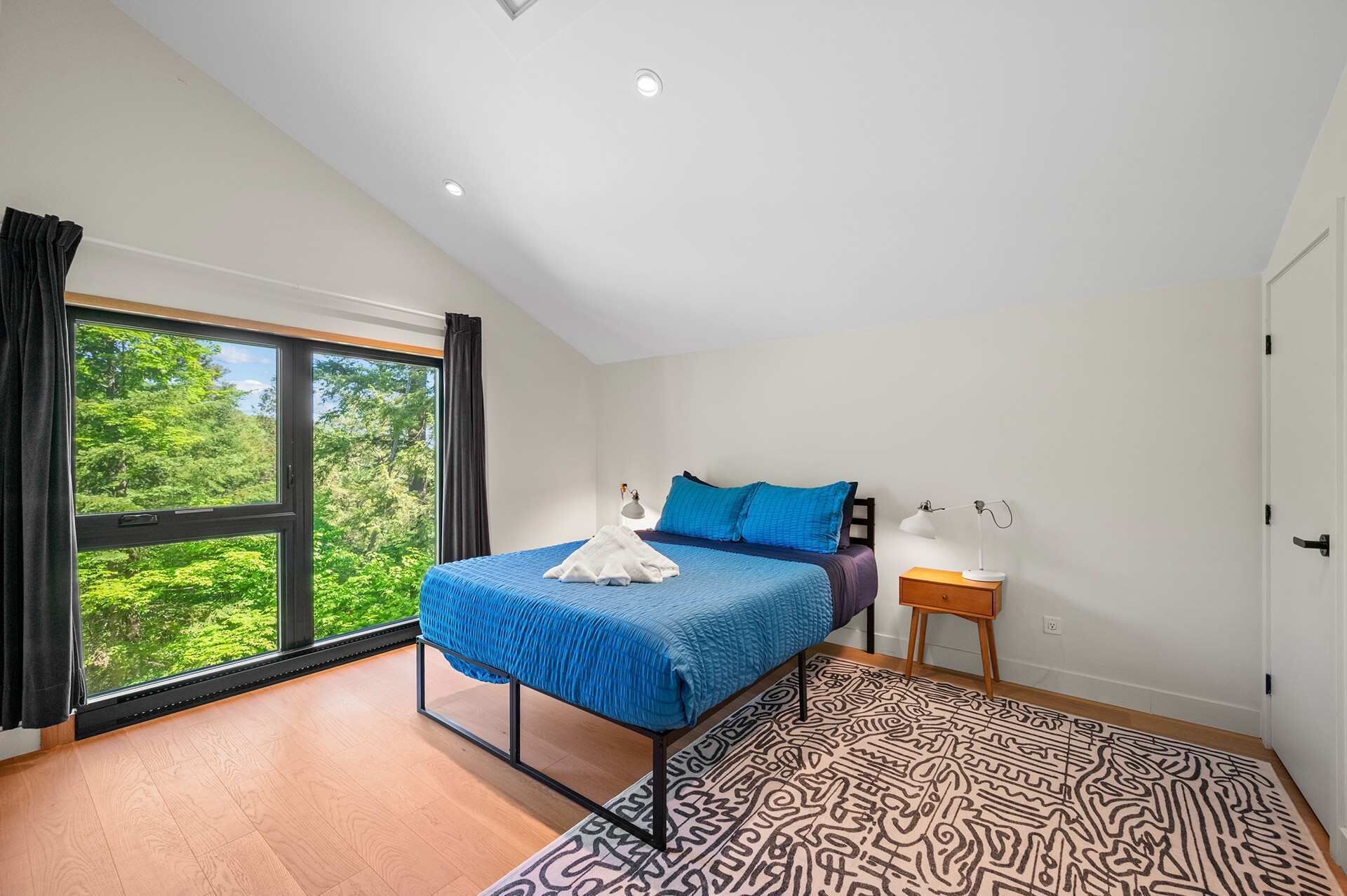 Un dormitorio con cama, mesita de noche, lámpara, ventana con cortinas y alfombra estampada.