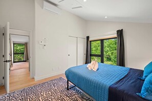 A bedroom with a large bed, a window with curtains, a door leading to another room, and a patterned rug. - Ambre (Grenville-sur-la-Rouge)