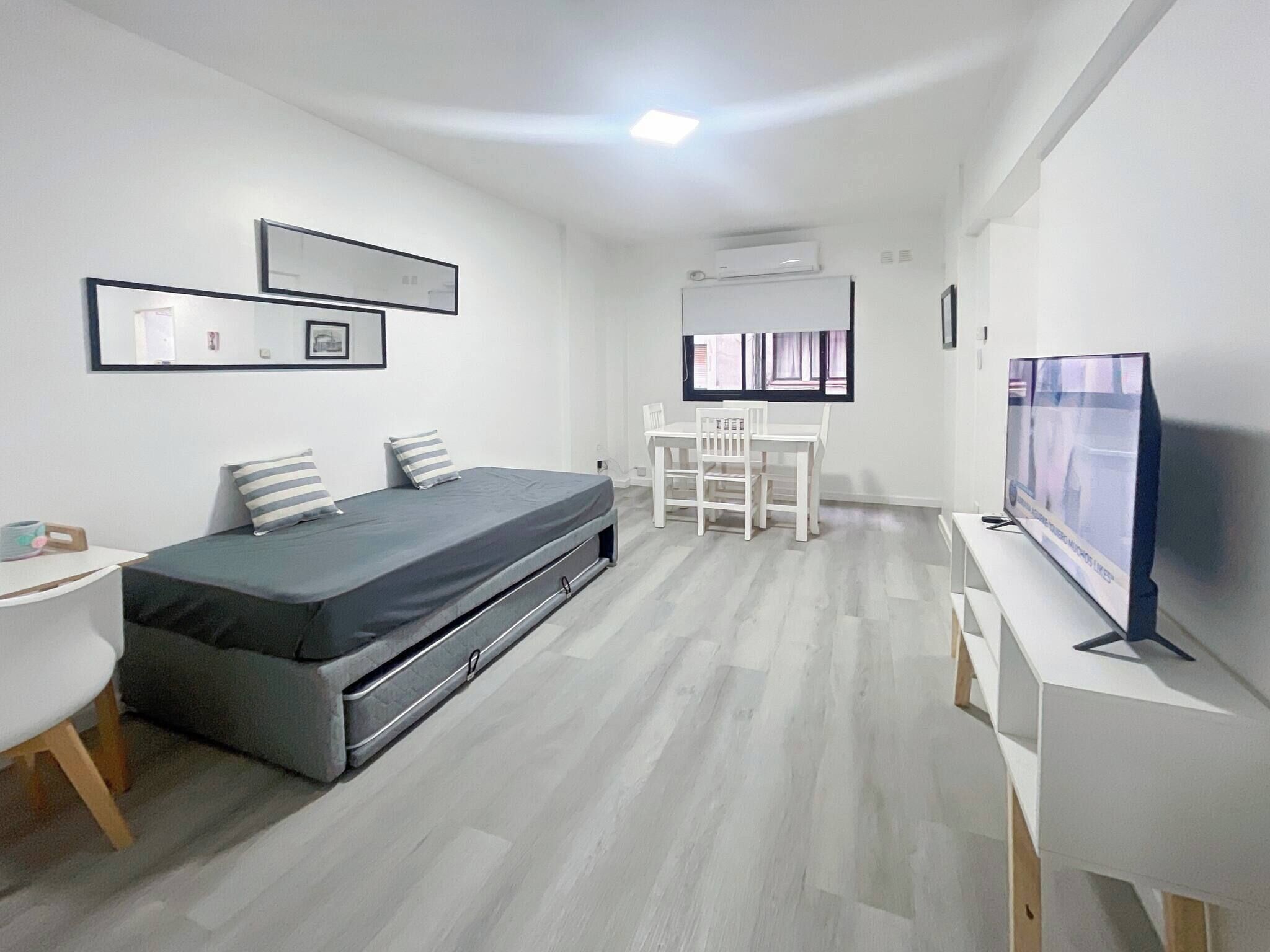 Un dormitorio moderno y minimalista con una cama, una mesita de noche y un televisor.