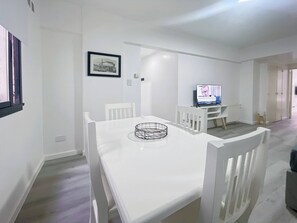A modern dining area with a white table and chairs, a framed picture on the wall, and a television in the background. - Charming Apartment in Recoleta 4 pax (Buenos Aires)