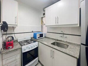 A compact kitchen with white cabinets, a gas stove, a microwave, and a sink. - Charming Apartment in Recoleta 4 pax (Buenos Aires)