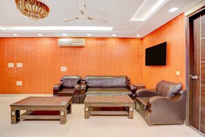 Un salon moderne comprenant un ensemble de canapés, deux tables basses, un ventilateur de plafond, un appareil de climatisation et un téléviseur à écran plat fixé au mur.