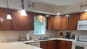 A kitchen with wooden cabinets, a large island, a stove, and a window with curtains. - Fabulous 3-bedroom house on 2 acres in quiet Garrett County wooded neighborhood (Frostburg)
