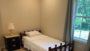 A single bed with a wooden frame and white bedding in a room with light wooden flooring and a nightstand with a lamp. - Fabulous 3-bedroom house on 2 acres in quiet Garrett County wooded neighborhood (Frostburg)
