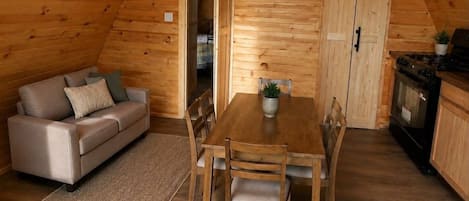 A cozy cabin interior with a sofa, dining table, chairs, a kitchen area with a stove, and a sliding door.