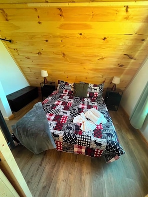 A bedroom with a wooden ceiling, a bed with a patterned bedspread, two bedside tables, and a bench. - Newly built cabin by Luray Caverns/Shenandoah Natl Park/Wedding Venues (Stanley)