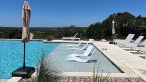Piscina azul límpida com espreguiçadeiras e guarda-sóis, em meio a uma área ajardinada com árvores.