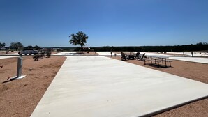 Uma área externa com um caminho pavimentado, mesas de piquenique e uma árvore.