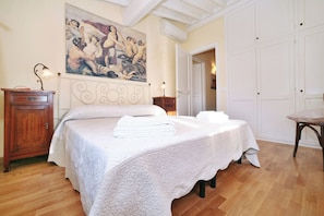 A bedroom with a bed, a wooden cabinet, a painting on the wall, and a door leading to another room. - Lucca: The Provincial Road. Wi-Fi, AC (Lucca)