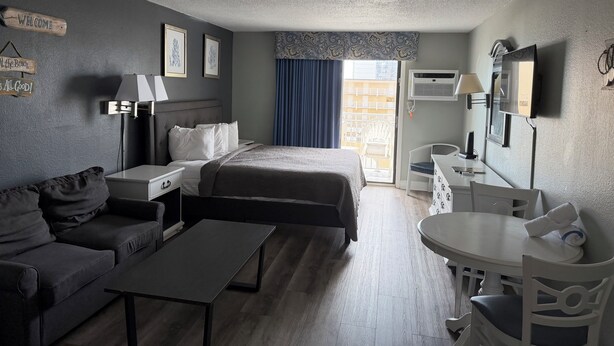 A hotel room with a bed, a sofa, a desk, a chair, a TV, and a balcony view. - Your Beachfront Getaway Awaits at Myrtle Beach SC (Myrtle Beach)