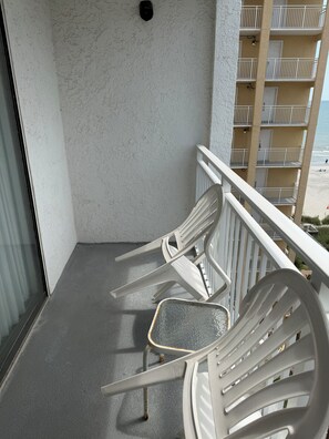 A balcony with white plastic chairs, a metal table, and a view of a beach and ocean. - Your Beachfront Getaway Awaits at Myrtle Beach SC (Myrtle Beach)