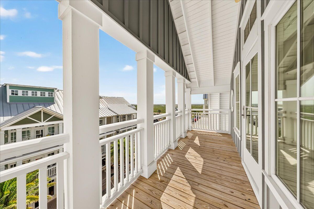 A covered wooden deck with white railings and large windows.