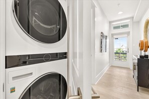 A laundry room with two stacked washing machines, a wooden cabinet, and a view of a balcony with plants. - Sea-cation TC 6303 (Port Aransas)