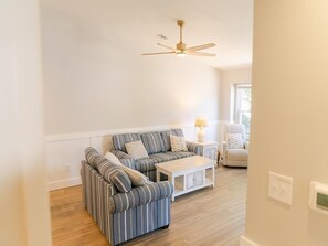 Ein Wohnzimmer mit einem gestreiften Sofa, einem weißen Couchtisch, einer Lampe und einem Deckenventilator.