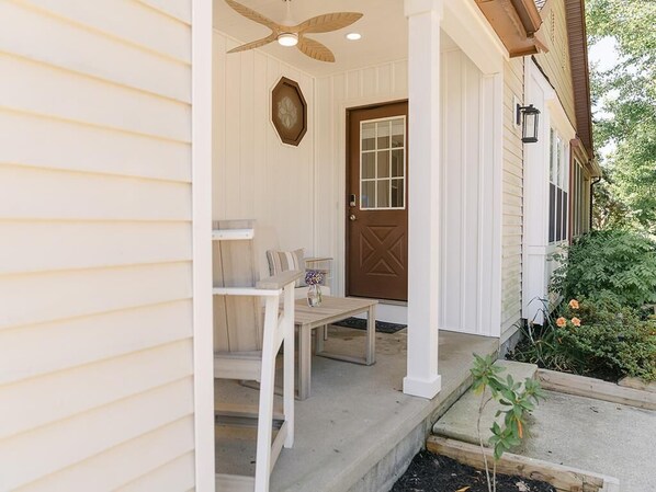 Eine Veranda mit Holztisch und -stühlen, einer braunen Tür und einem Deckenventilator.
