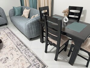A living room with a grey sofa, a dining table with chairs, a vase with dried flowers, and a patterned rug. - Fantastic 3-bedroom apartment in Embakasi Nairobi perfect for your stay (Embakasi, nairobi)