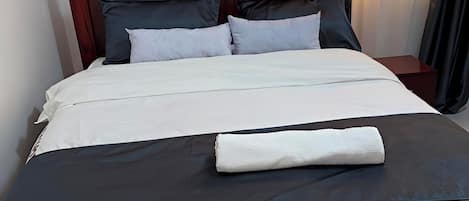 Una cama bien tendida con una colcha blanca y oscura, una almohada blanca y una toalla blanca doblada encima.