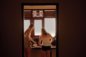 Two individuals in a kitchen with a window and a decorative screen.