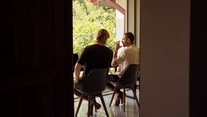 Two people seated at a table with a view of greenery outside a window.
