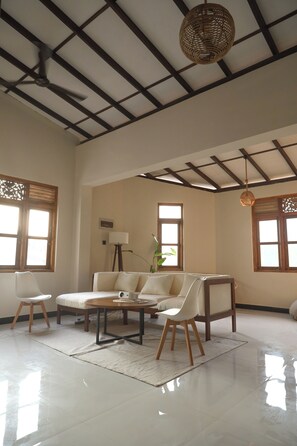 A spacious living room with a high ceiling, a sofa set, a coffee table, and a floor lamp.