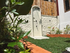 Une porte blanche avec une petite fenêtre, entourée d’un jardin avec de l’herbe verte et des plantes.