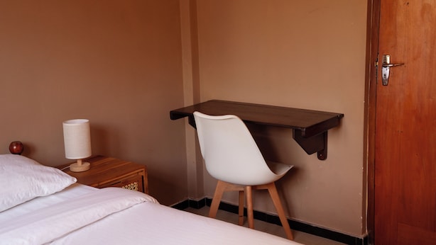 A hotel room with a bed, a desk with a chair, a lamp, and a door.
