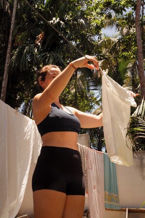 A person hanging clothes on a line outdoors with palm trees in the background.