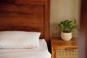 A bed with white bedding, a wooden headboard, a bedside table with a woven basket, and a potted plant.