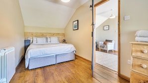 A bedroom with a wooden headboard, a bed with a grey bedspread, a wooden dresser, and a mirror reflecting a dining area.