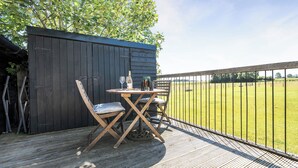 An outdoor patio with a table and chairs, a fence, and a view of a grassy field.
