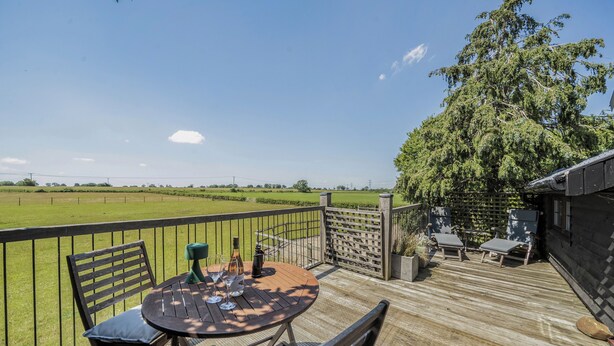 A wooden deck with a table and chairs, a view of a green field, and a large tree.