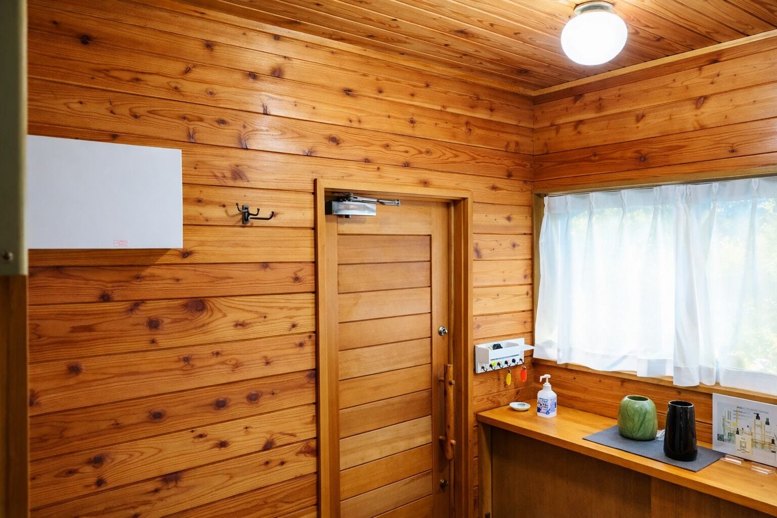 Ein Holzblockhaus-Innenraum mit Tür, Fenster mit Vorhängen, einem Waschbecken und Pflegeprodukten.