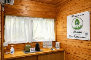 Interior de una cabaña de madera con una mesa de recepción, un letrero de bienvenida, una ventana con cortinas y un dispensador de gel antibacterial.