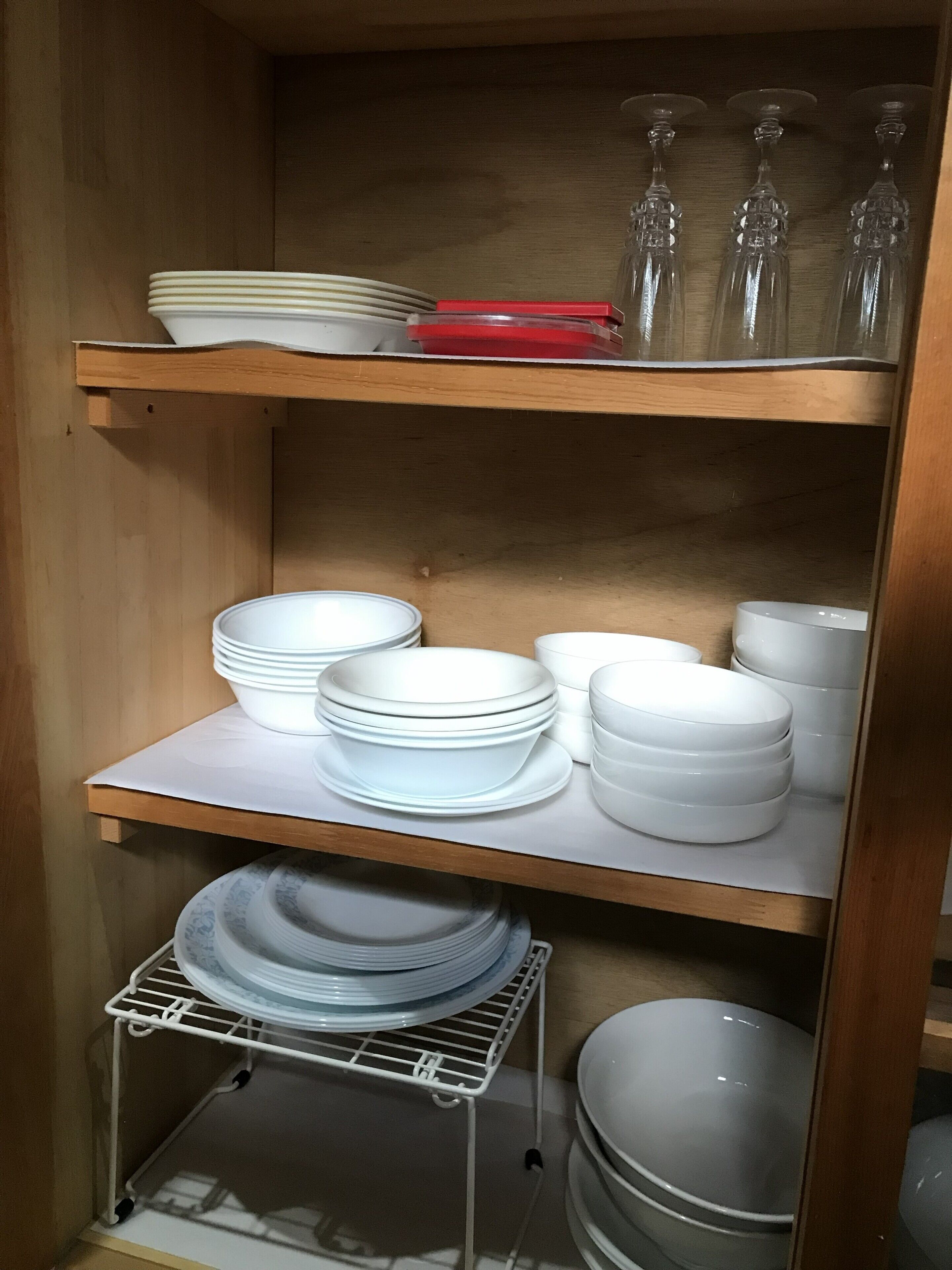 Una repisa de cocina con platos y tazones blancos apilados, y un escurreplatos blanco.