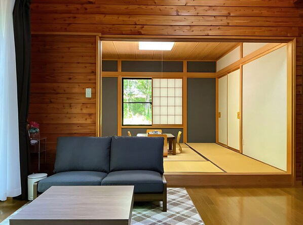 A traditional Japanese room with tatami flooring, a low table with a cushion, and a sliding door.