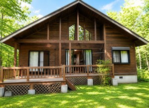 A two-story wooden cabin with a deck, surrounded by lush greenery.