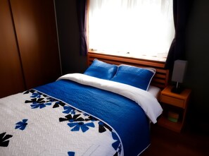 A bed with a blue and white bedspread, a wooden headboard, and a bedside table with a lamp.