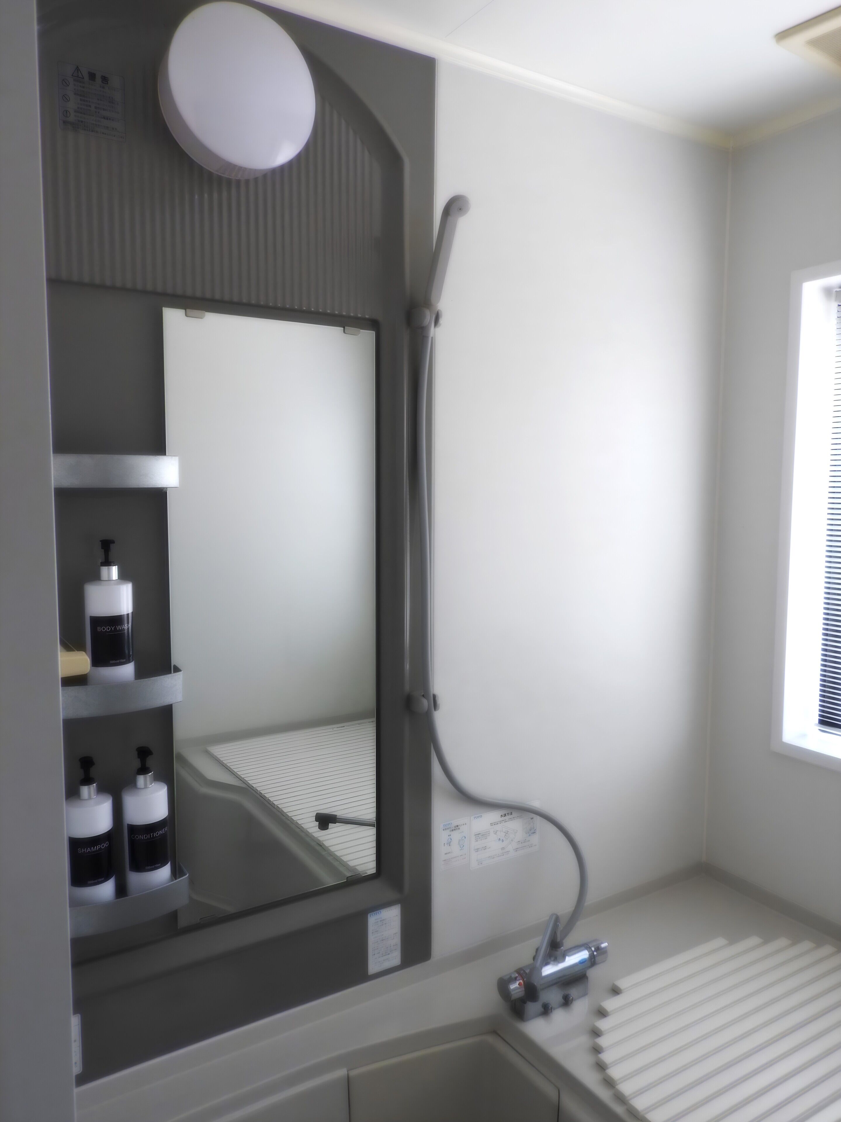 Een badkamer met een douche, een spiegel en schapjes met toiletartikelen.