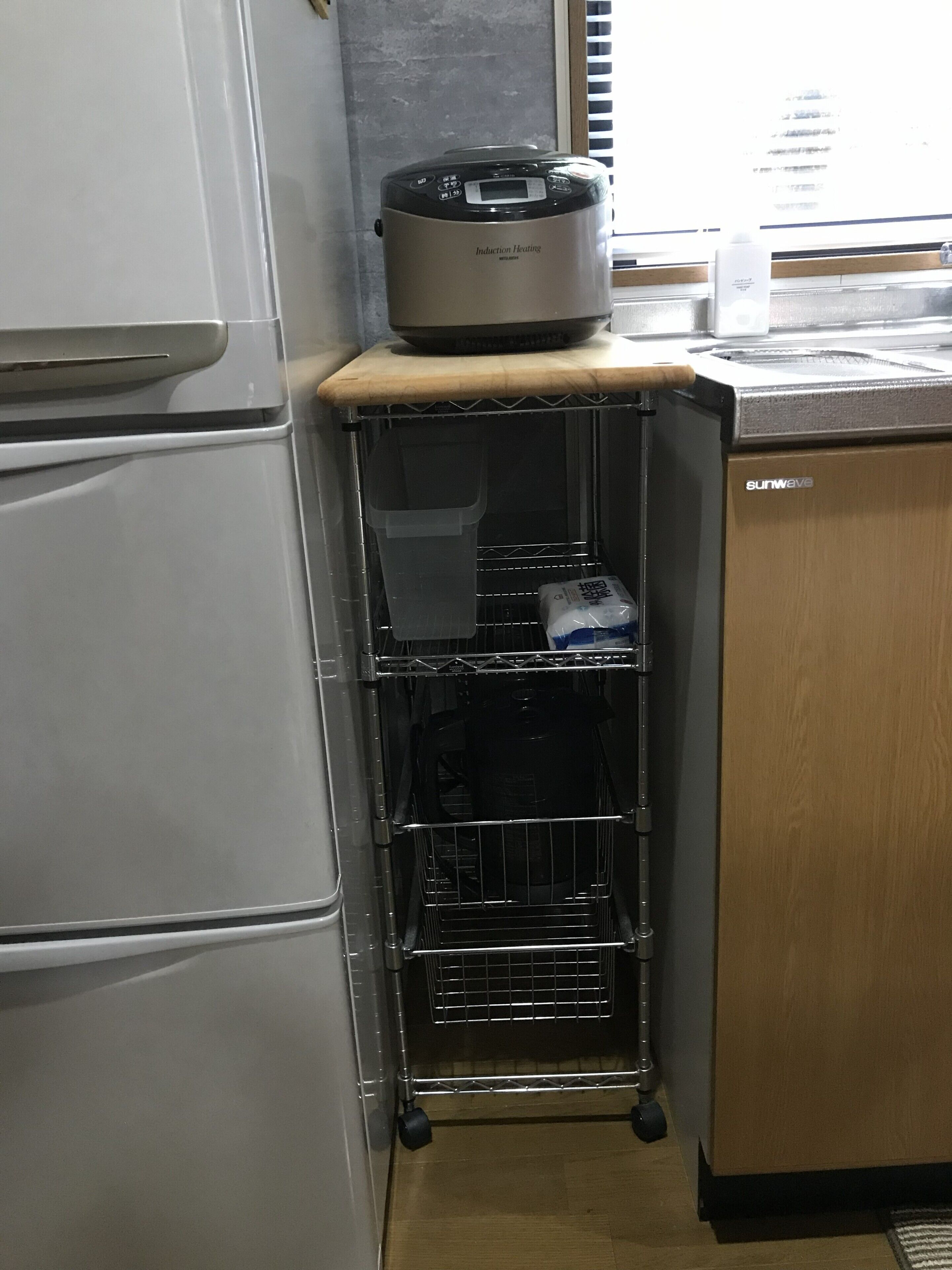 Ett kök med ett vitt kylskåp, en induktionshäll i rostfritt stål och ett träskåp.